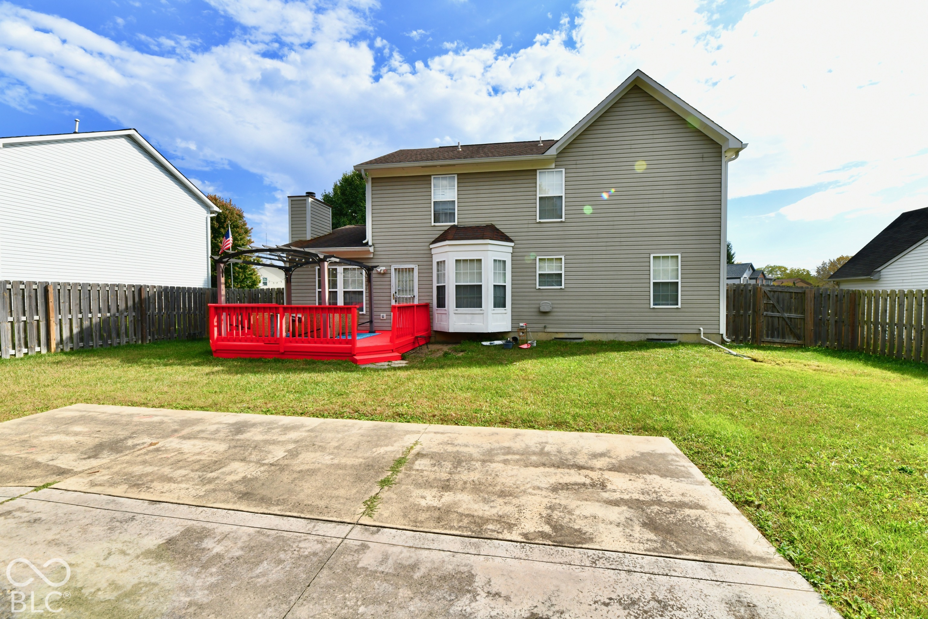 Two-story exterior with horizontal siding, a bay window, a raised deck, a concrete patio, and a fenced yard