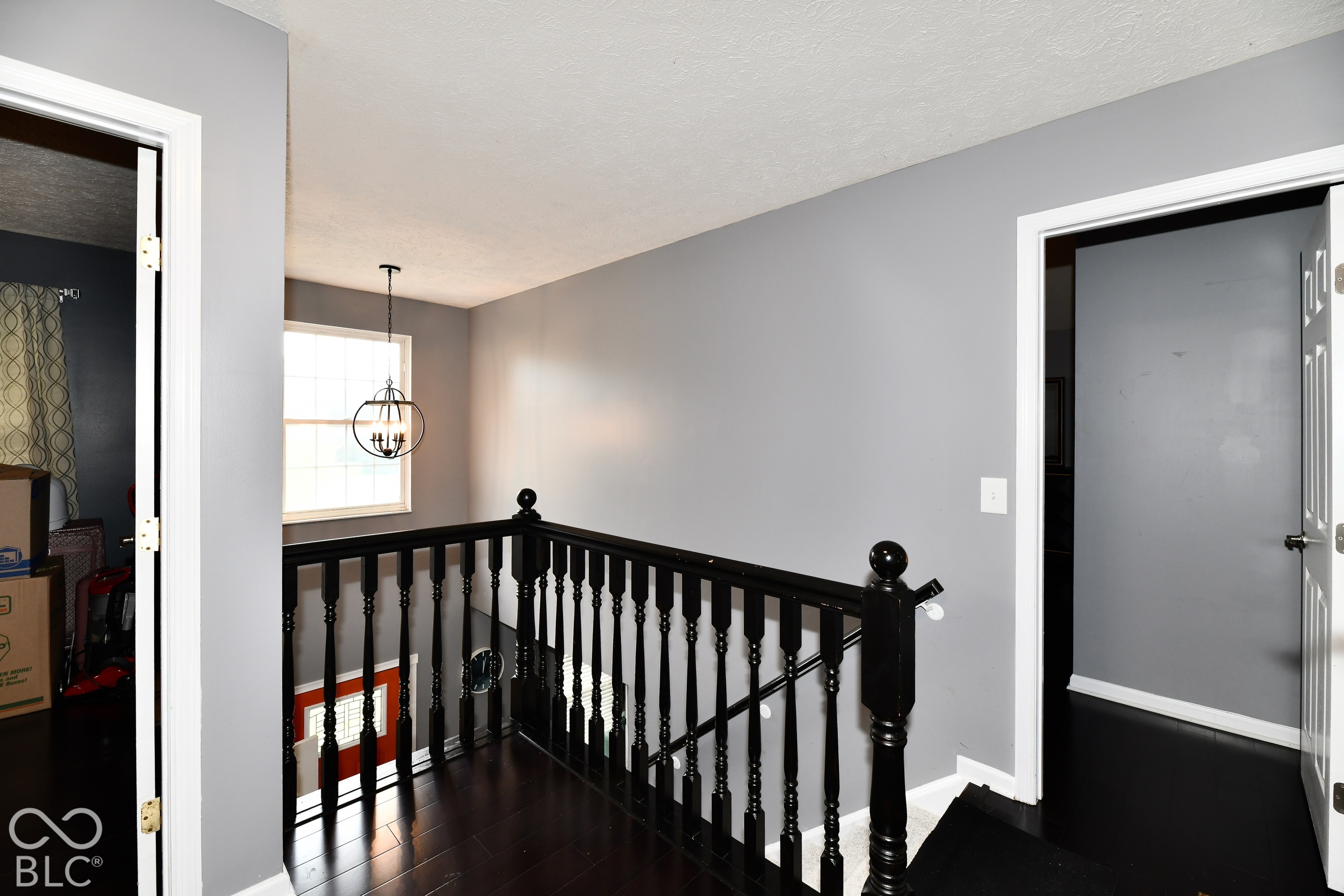 Landing featuring dark-stained wood-finish flooring, a black-painted wooden balustrade, and a hanging orb-style pendant light