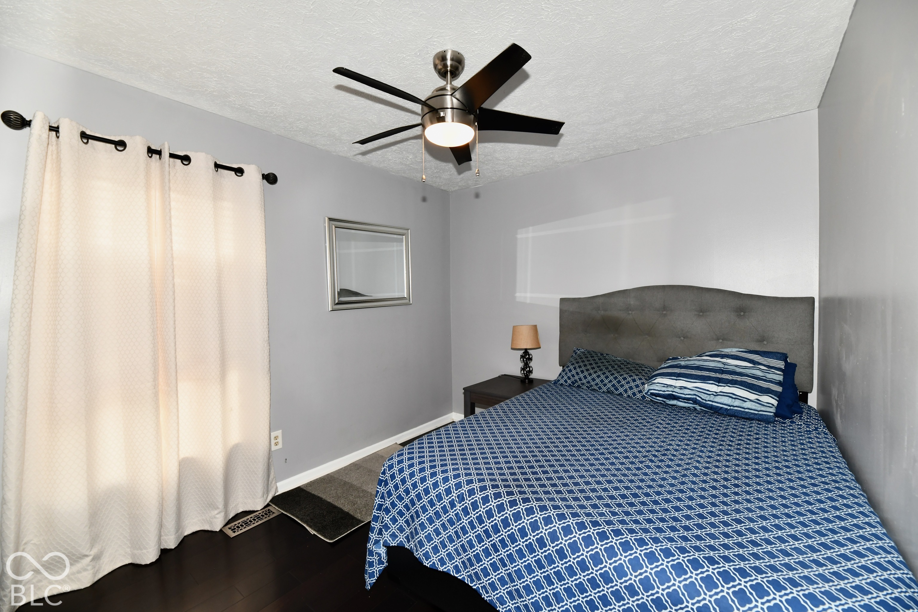 Room featuring wood-finish flooring, a brushed-nickel ceiling fan with integrated lighting, and a wall-mounted mirror