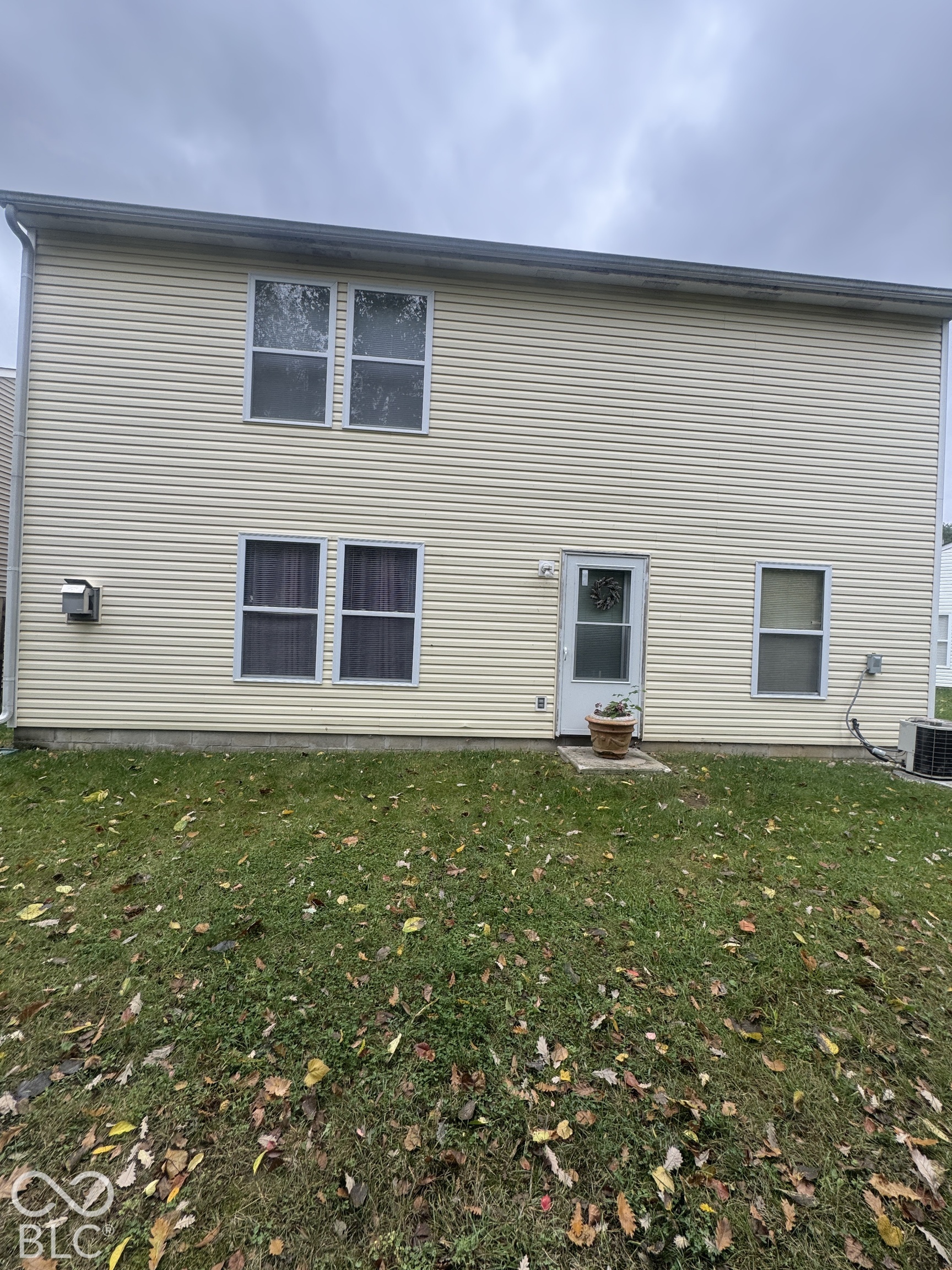 Two-story exterior featuring cream-colored vinyl siding, five double-hung windows, and a dedicated rear entry door with a concrete stoop