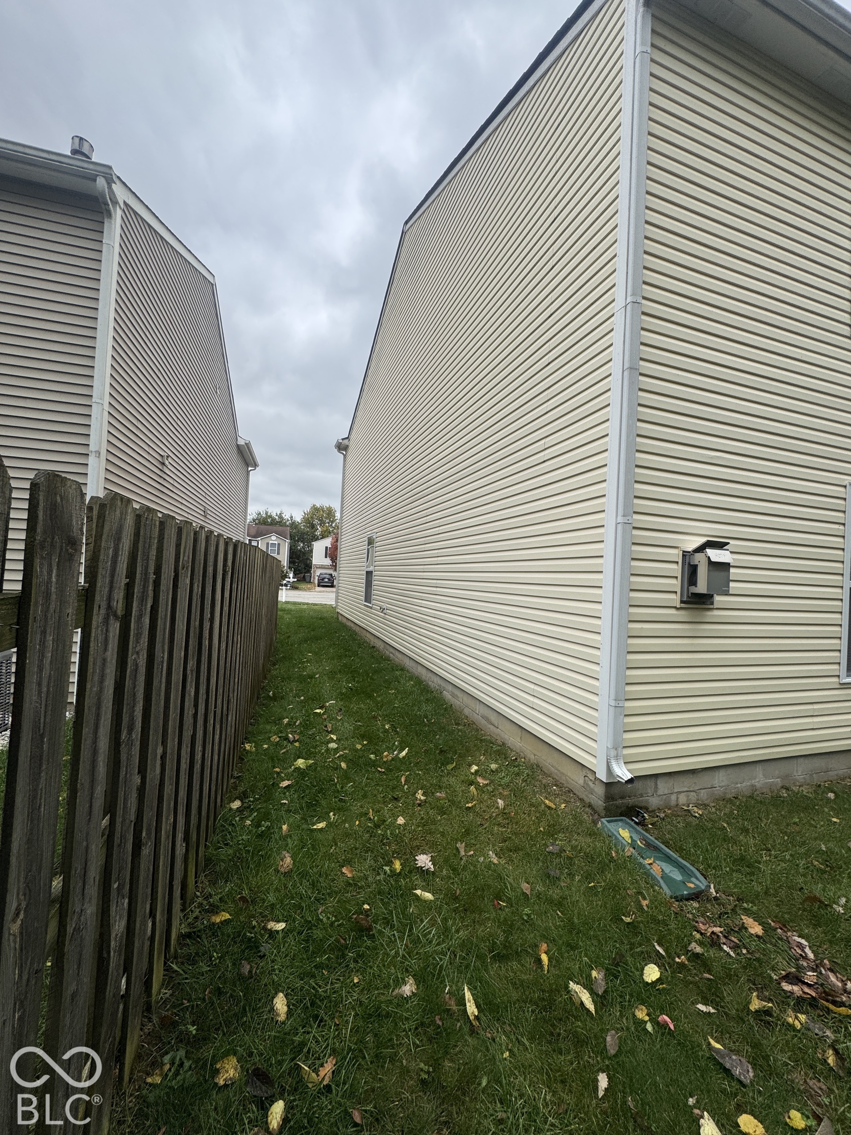 Exterior side elevation featuring light-colored horizontal vinyl siding, white downspouts, and a wood privacy fence