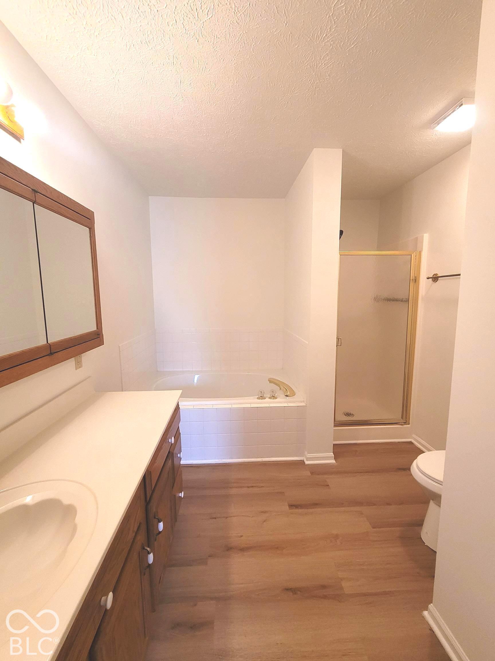 Bathroom featuring wood-finish flooring, a soaking tub with tile surround, a glass-enclosed shower, wood-tone vanity cabinetry, and a medicine cabinet