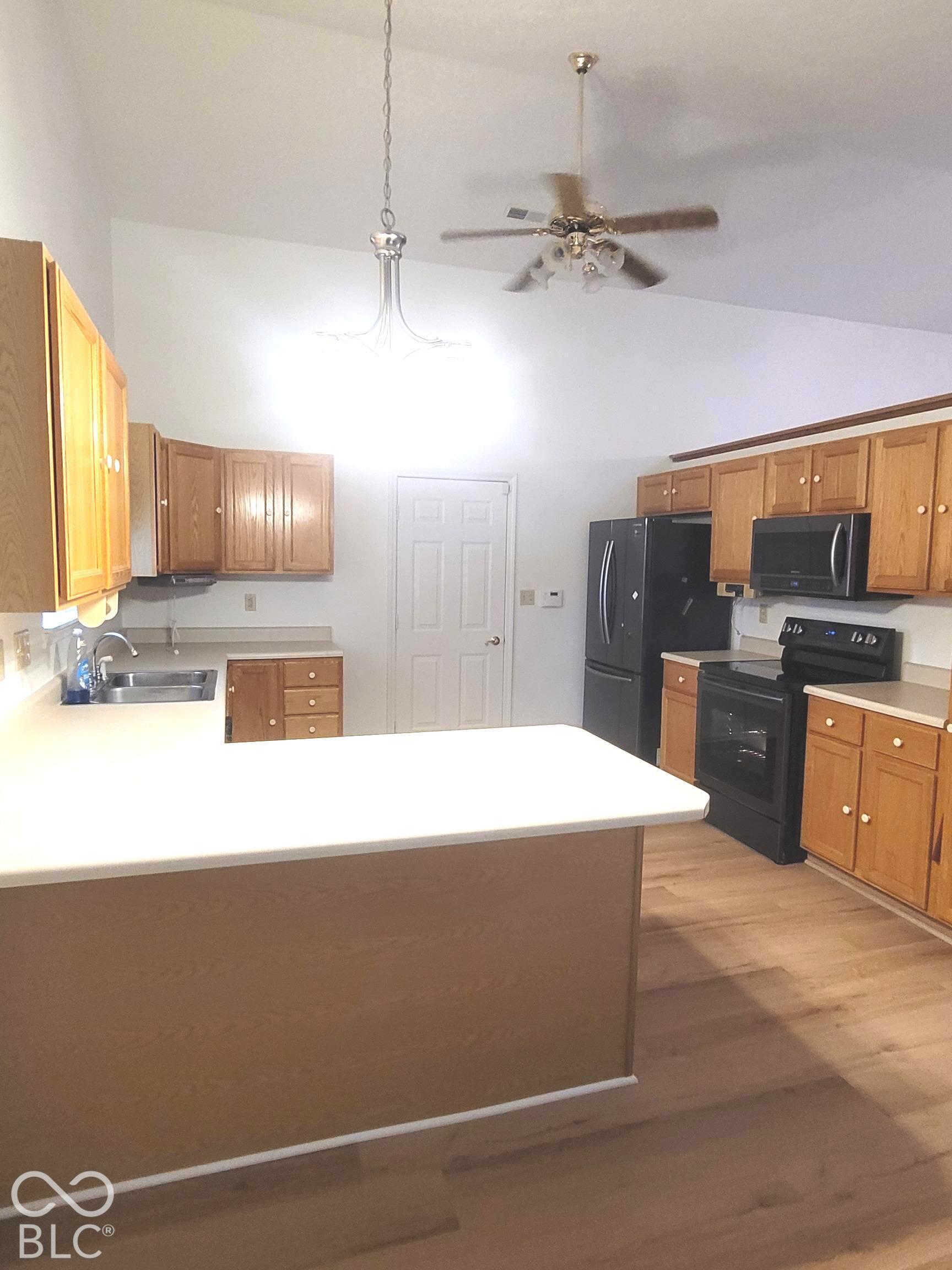 Kitchen featuring wood cabinetry, a peninsula with a solid-surface countertop, vaulted ceilings, and wood-finish flooring