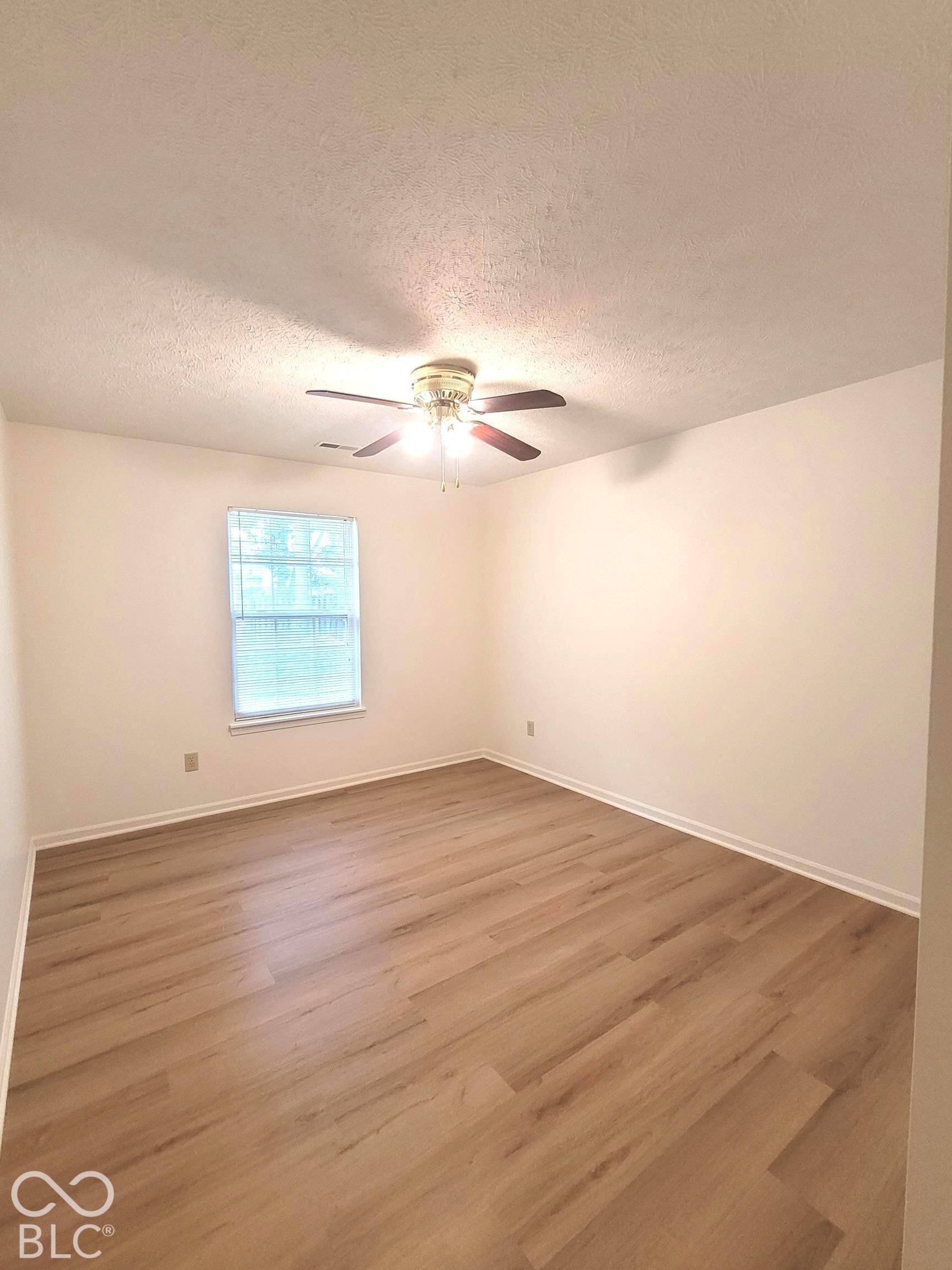 Neutral-toned interior featuring wood-finish flooring, a ceiling fan with integrated lighting, and a single-pane window