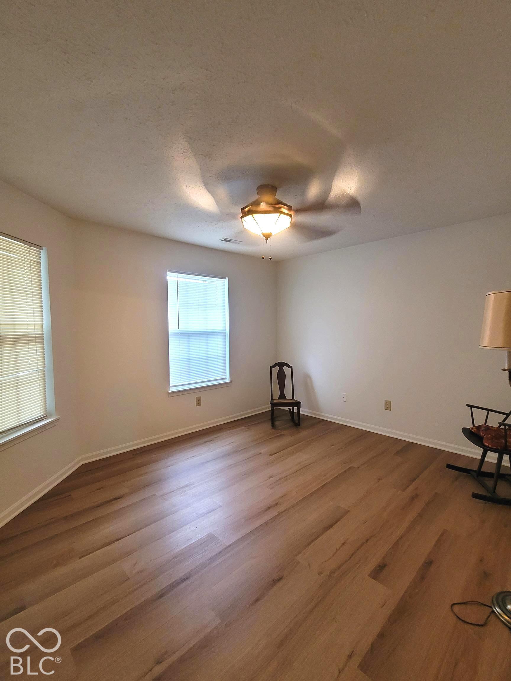 Wood-finish flooring, neutral wall tones, multi-pane windows, and a central ceiling fan with integrated light fixture