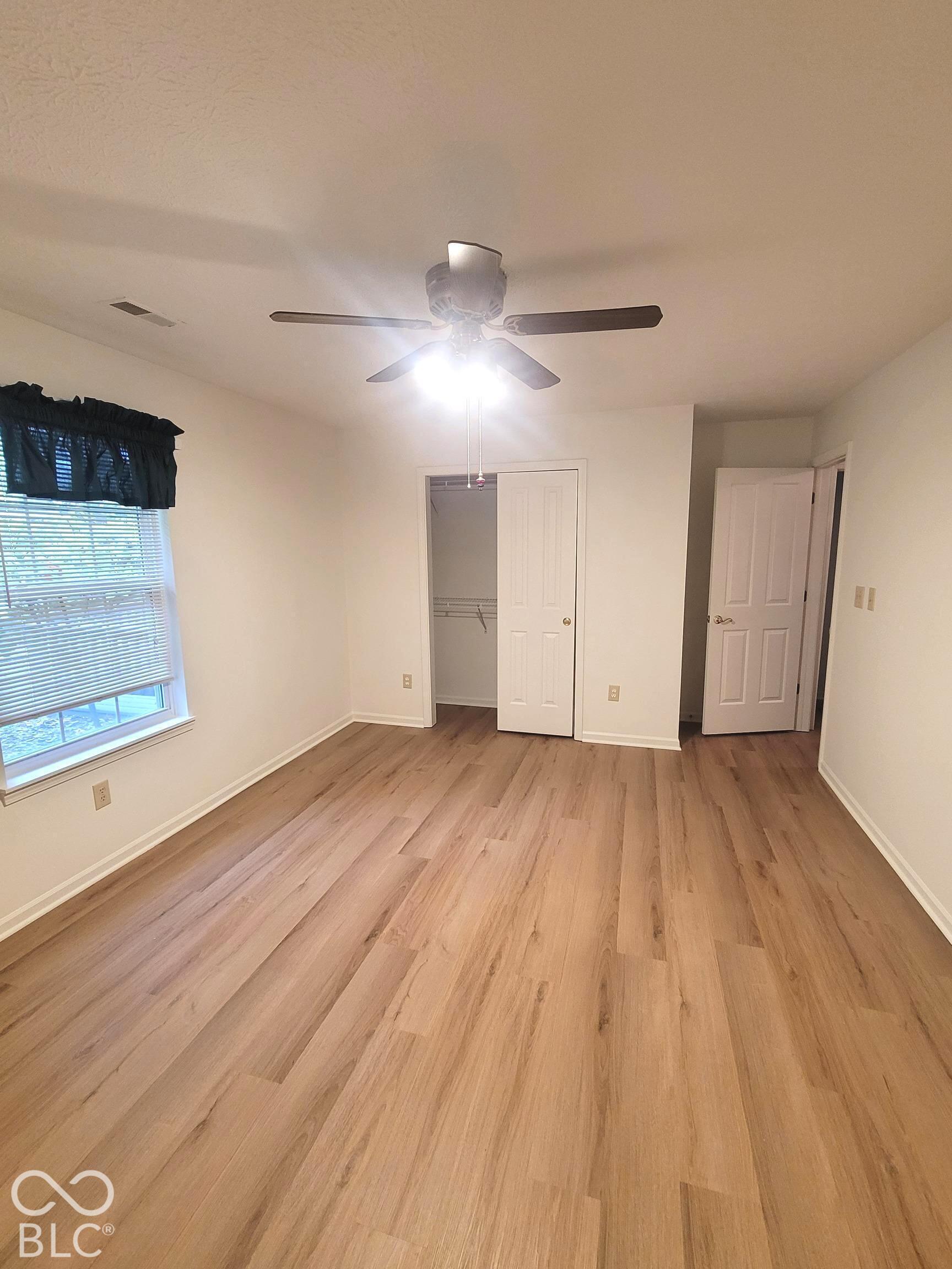Virtually Altered - Room featuring wood-finish flooring, a ceiling fan with integrated lighting, a single window, and a built-in closet with panel doors