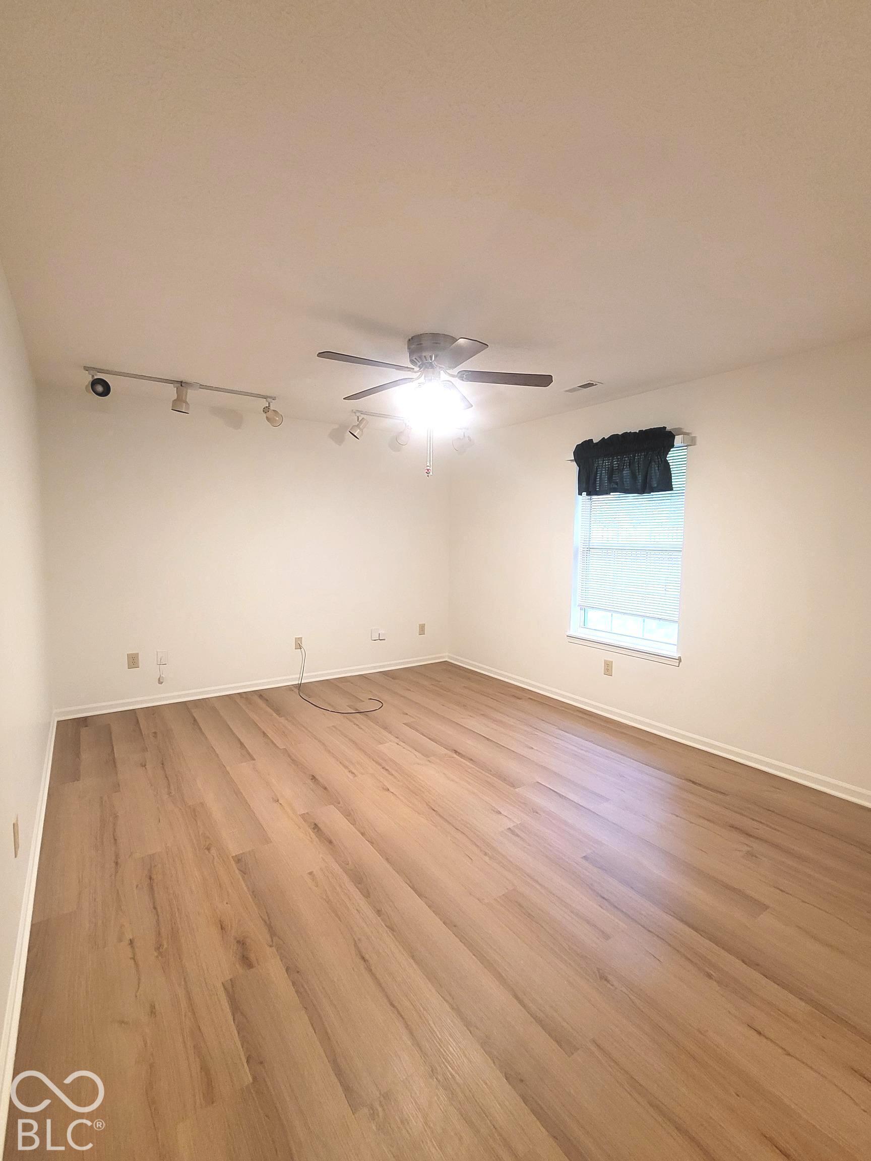 Virtually Altered - Room featuring wood-finish flooring, a multi-head track lighting system, and a ceiling fan with integrated light