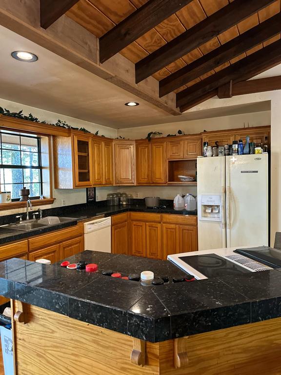 Kitchen featuring vaulted ceiling with beams, sink, white appliances, a kitchen island, and a kitchen breakfast bar