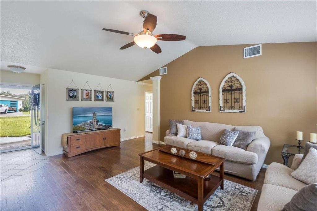 Living area with lofted ceiling, visible vents, ornate columns, and wood finished floors
