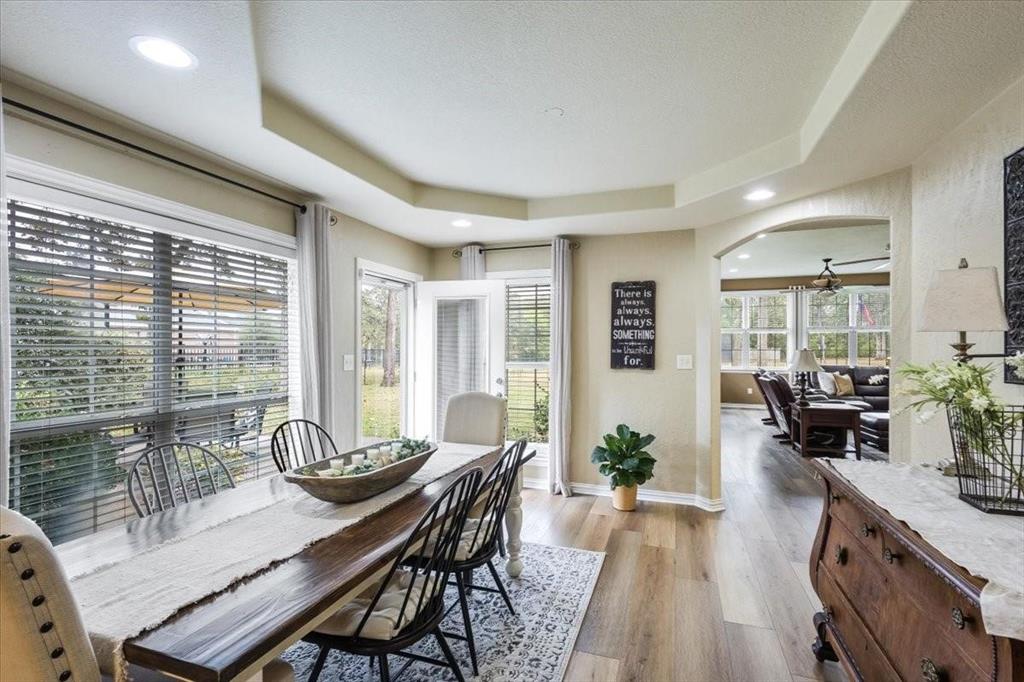 Dining room with arched walkways, a textured ceiling, baseboards, light wood finished floors, and a raised ceiling