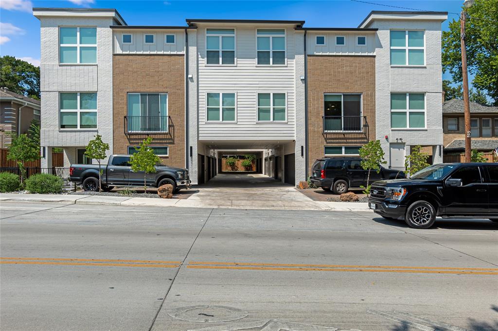 Multi-story exterior featuring a mix of brick and horizontal siding, oversized windows, private balconies with metal railings, and a covered ground-level drive-through