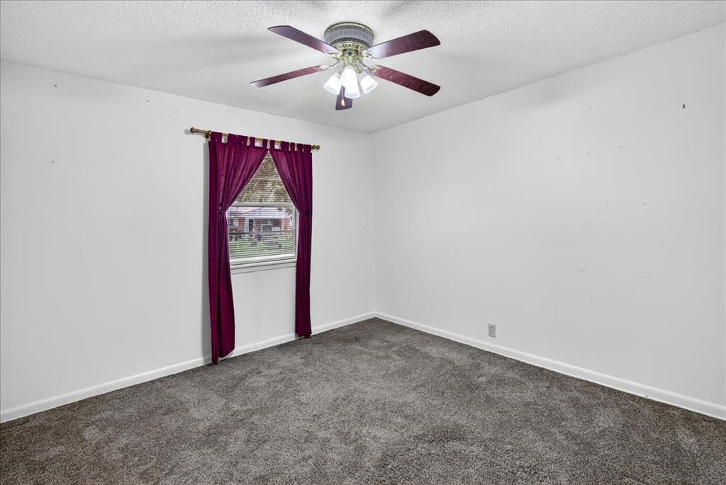 Empty room featuring dark carpet, a textured ceiling, and ceiling fan