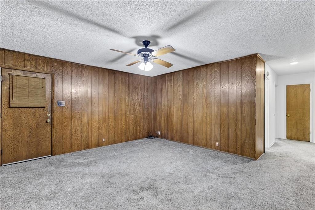 Empty room featuring light carpet, wooden walls, a textured ceiling, and a ceiling fan