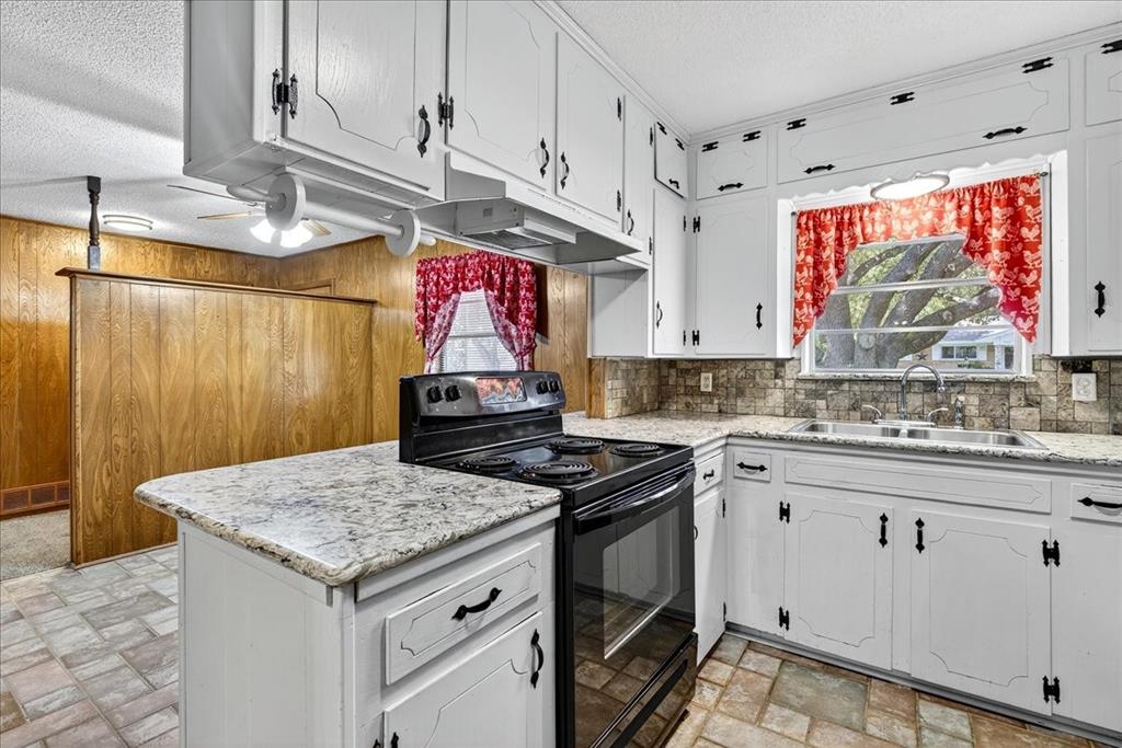 Kitchen with white cabinets, black range with electric stovetop, a textured ceiling, wooden walls, and under cabinet range hood