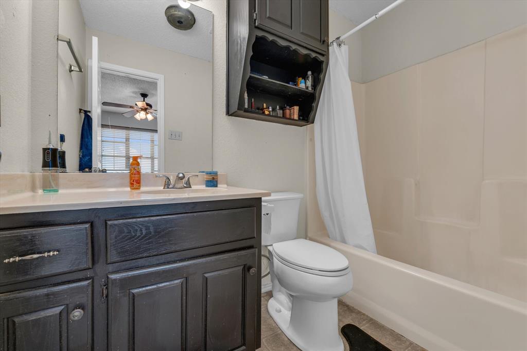 Full bath featuring shower / bath combo, vanity, light tile patterned floors, a textured ceiling, and ceiling fan