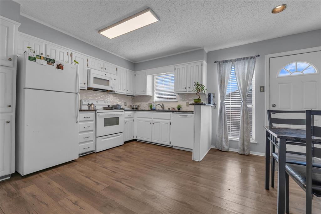 Kitchen with white appliances, white cabinetry, dark wood-type flooring, backsplash, and a textured ceiling