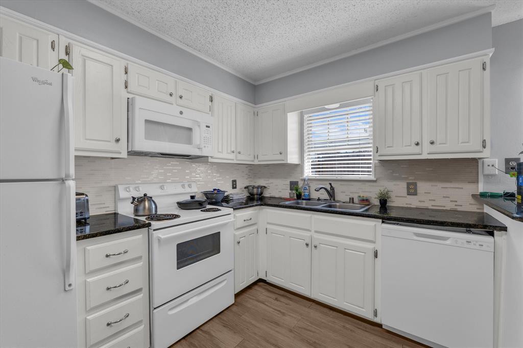 Kitchen featuring white appliances, white cabinetry, tasteful backsplash, light wood finished floors, and dark stone counters