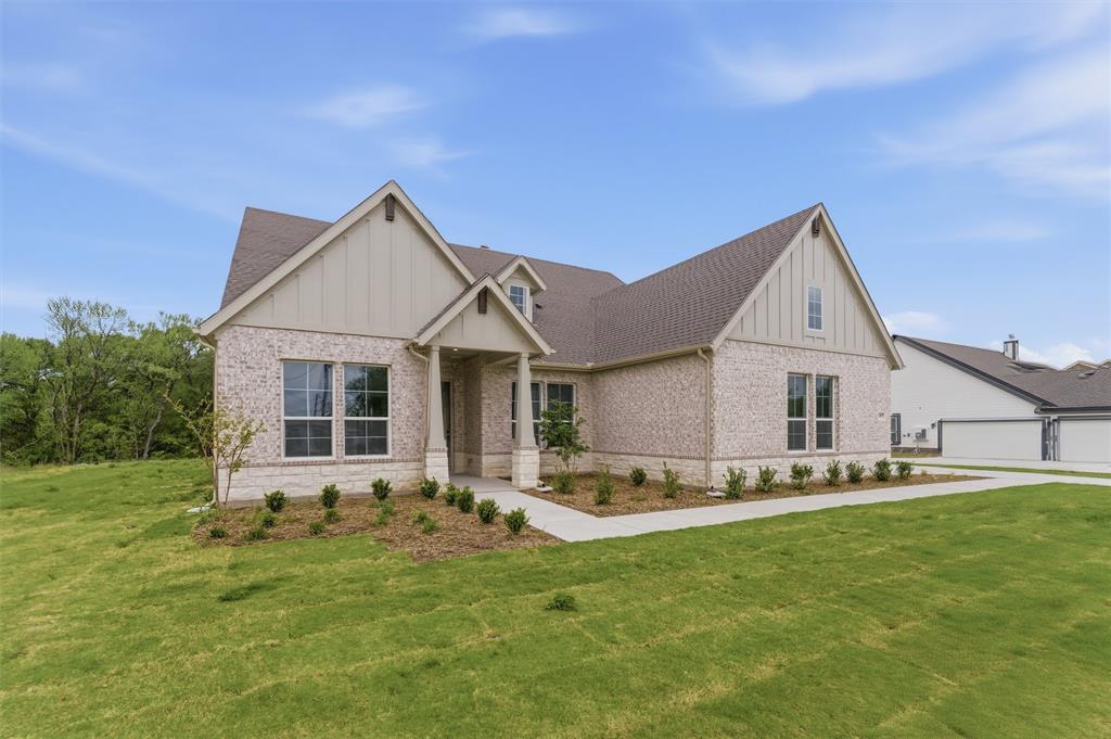View of front of property featuring board and batten siding, brick siding, a front yard, and roof with shingles