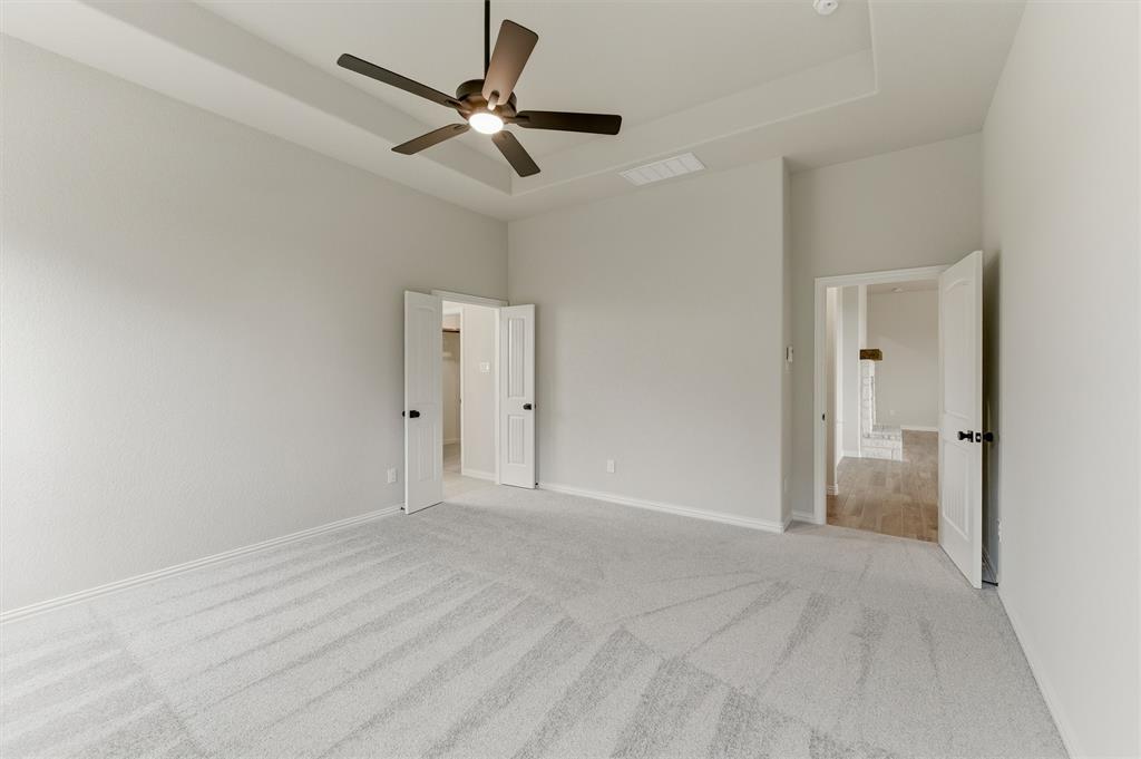 Unfurnished bedroom featuring a tray ceiling, a ceiling fan, light carpet, and ensuite bathroom