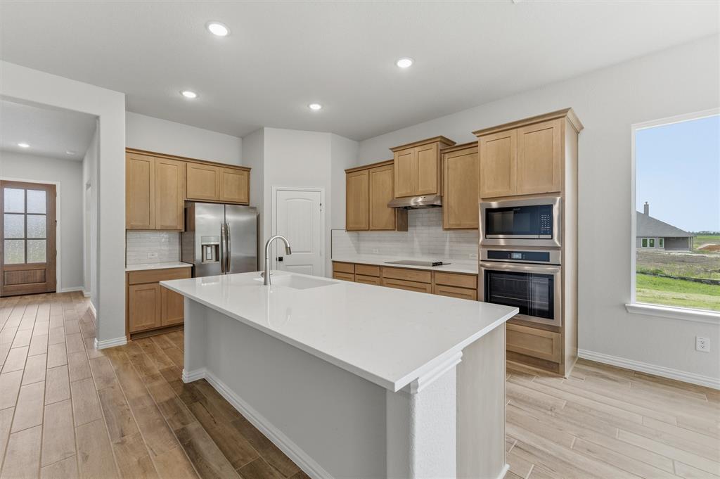 Kitchen featuring stainless steel appliances, an island with sink, decorative backsplash, light wood-style floors, and recessed lighting