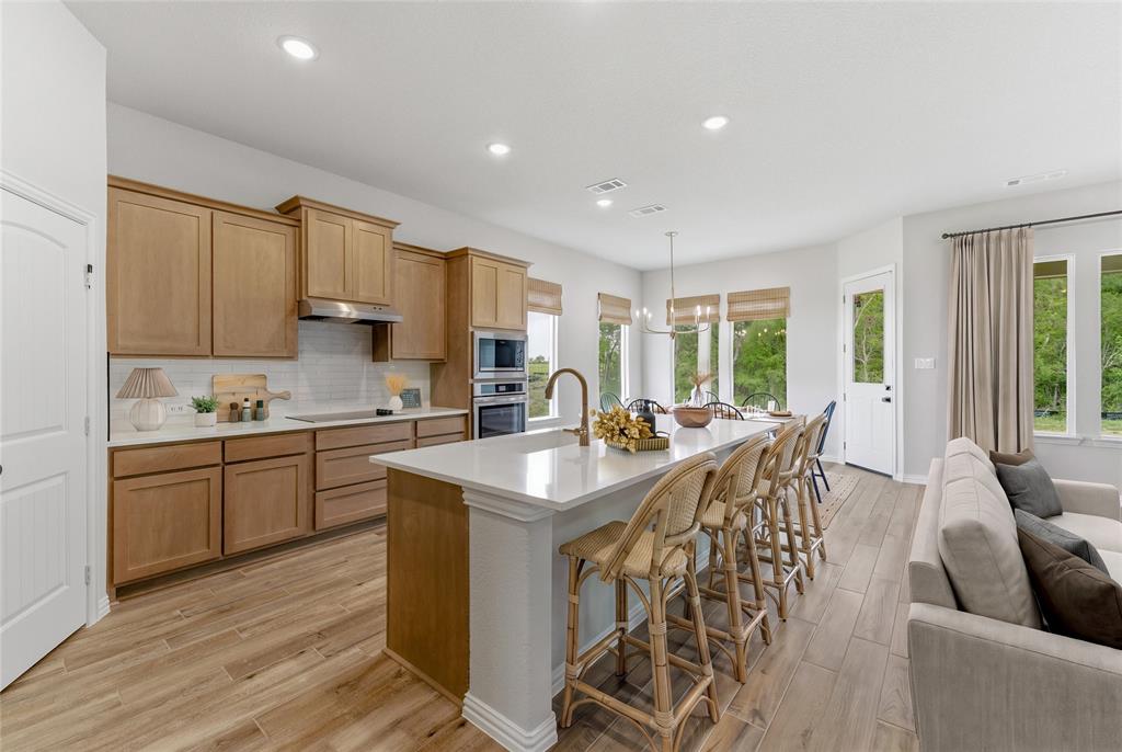 Open-concept kitchen and living area featuring wood-finish flooring, recessed lighting, and a white tile backsplash