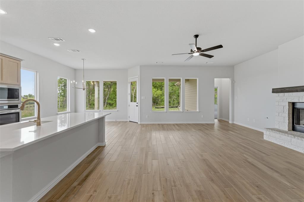 Unfurnished living room featuring a fireplace with raised hearth, light wood finished floors, suspended lighting, and a ceiling fan
