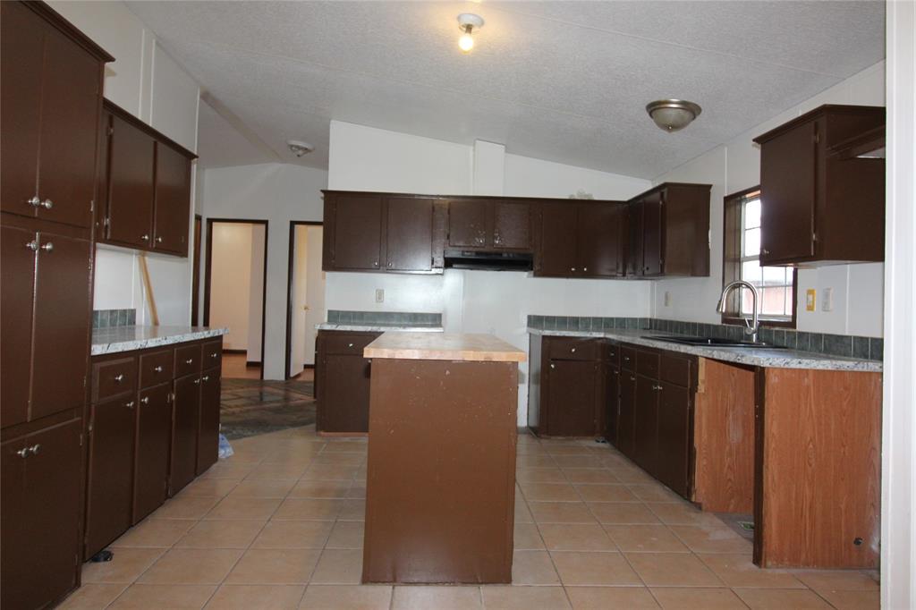 Kitchen with vaulted ceiling, a kitchen island, light countertops, dark brown cabinets, and light tile patterned floors