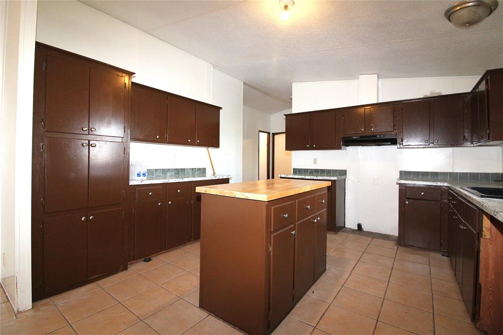 Kitchen with dark brown cabinetry, light tile patterned flooring, a kitchen island, lofted ceiling, and under cabinet range hood