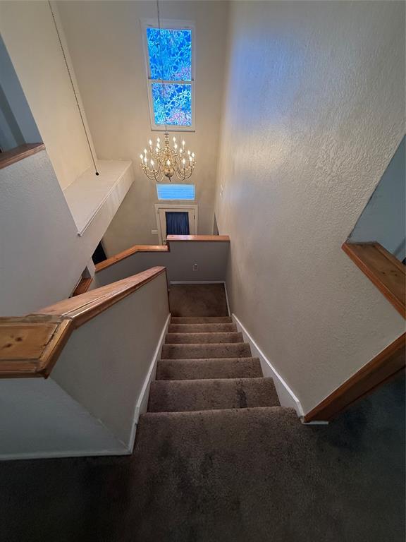 Stairs featuring carpet floors, a textured wall, and a chandelier