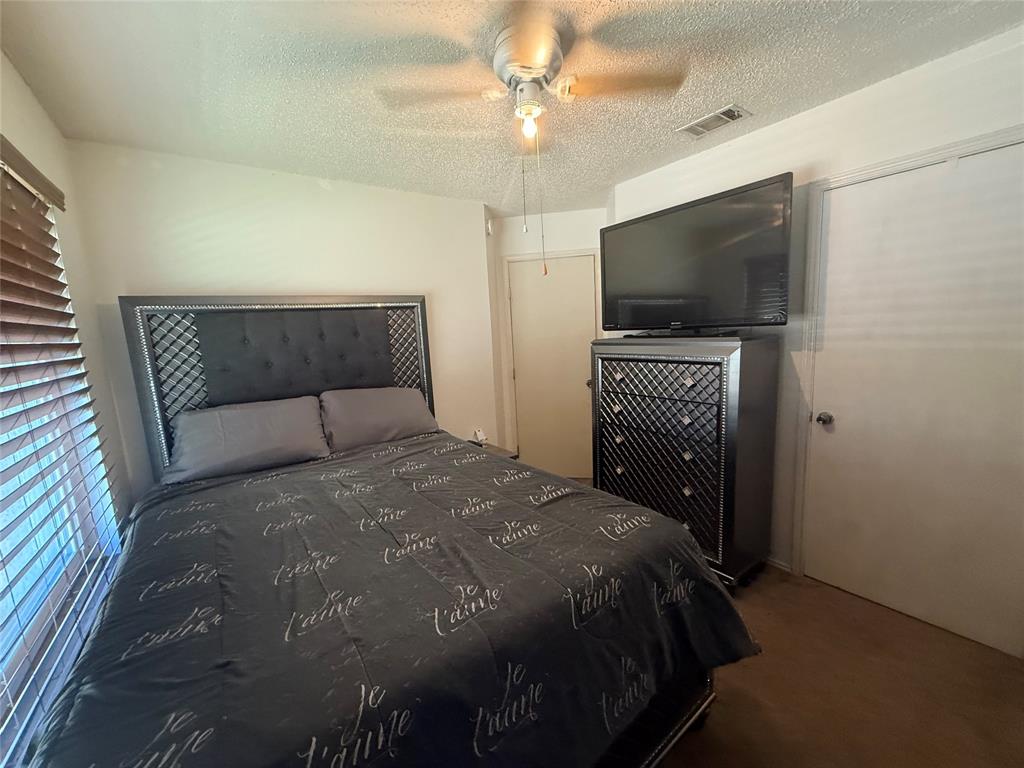 Bedroom with a textured ceiling, ceiling fan, and dark colored carpet
