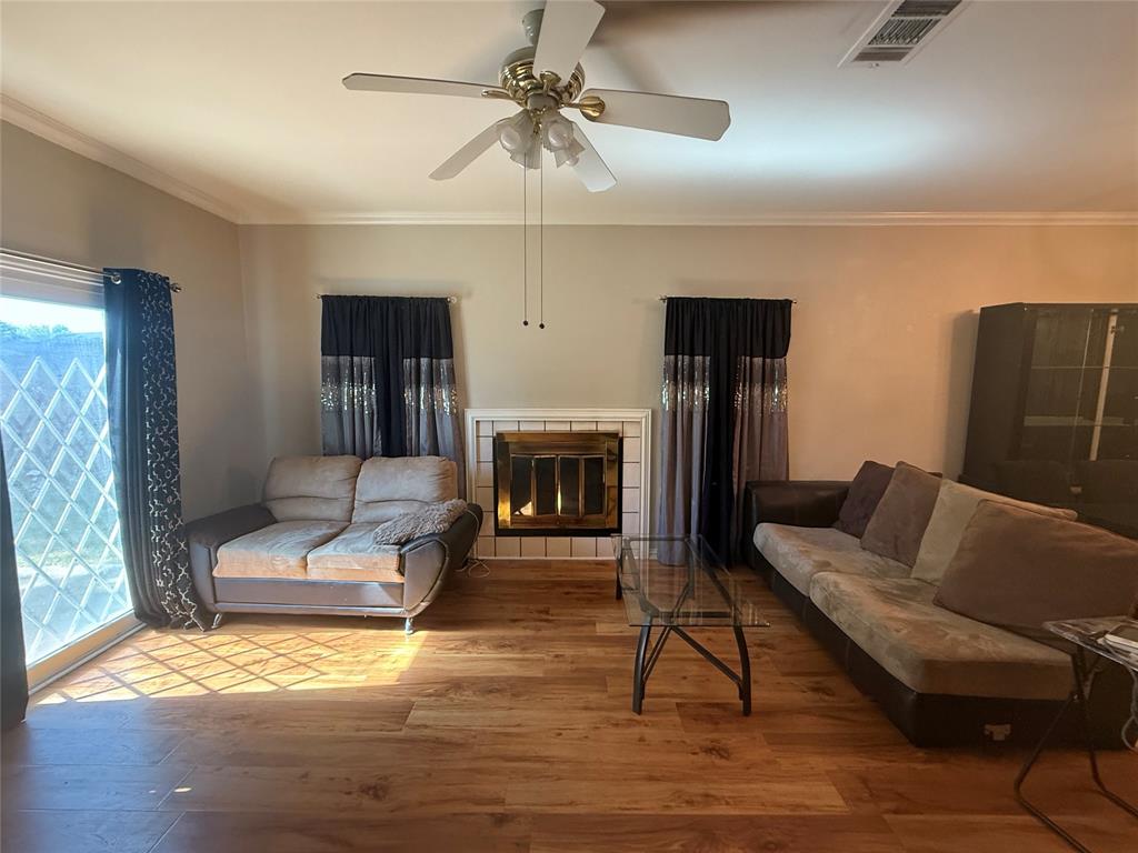 Living room with ornamental molding, a tile fireplace, wood finished floors, and a ceiling fan