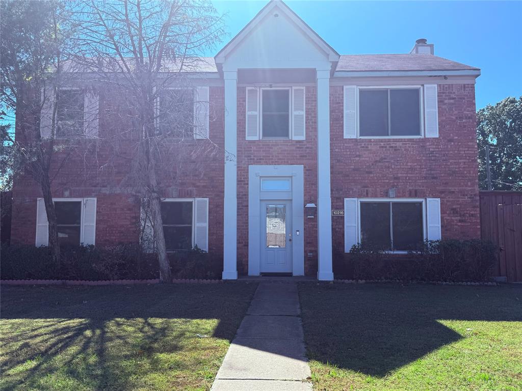 View of front of property featuring a front yard, brick siding, and a chimney