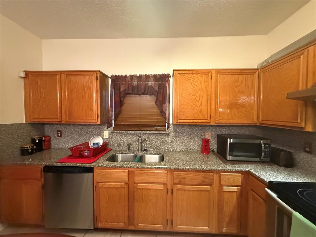 Kitchen featuring stainless steel appliances, decorative backsplash, brown cabinetry, light stone counters, and a textured ceiling