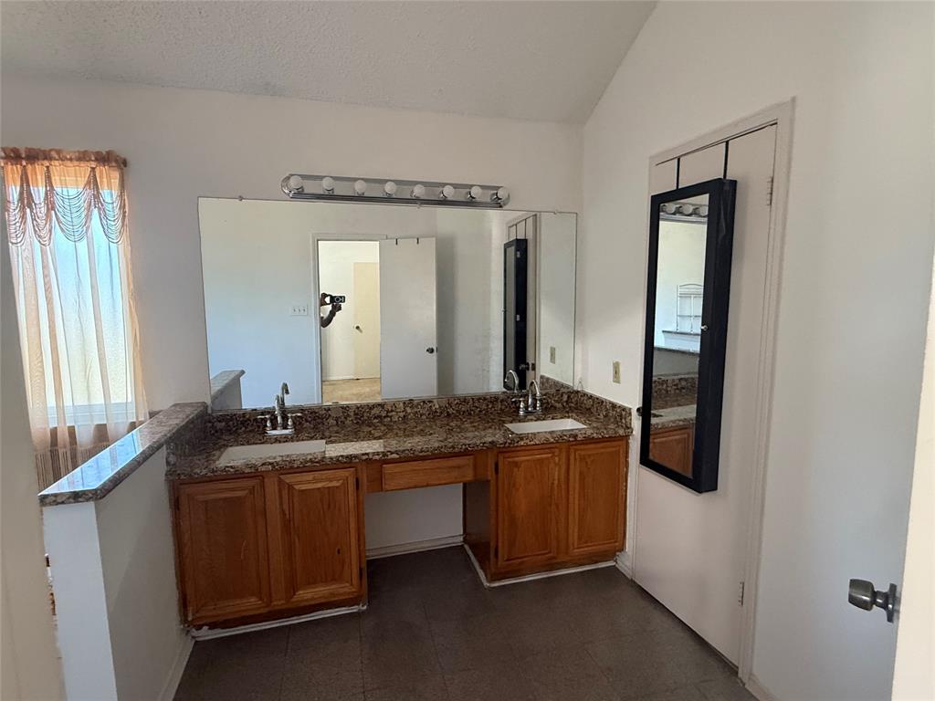 Full bathroom featuring double vanity, a textured ceiling, and lofted ceiling