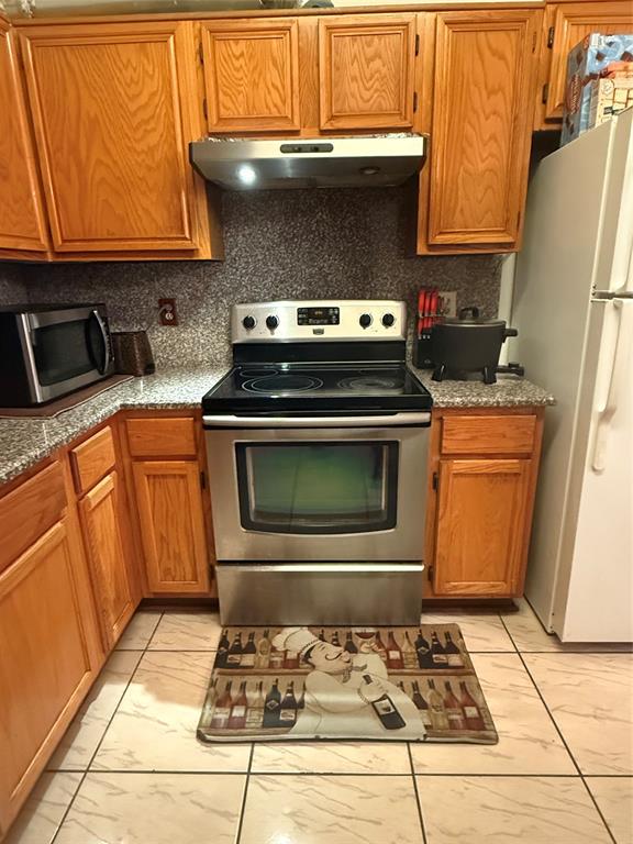 Kitchen featuring stainless steel appliances, tasteful backsplash, brown cabinets, and range hood