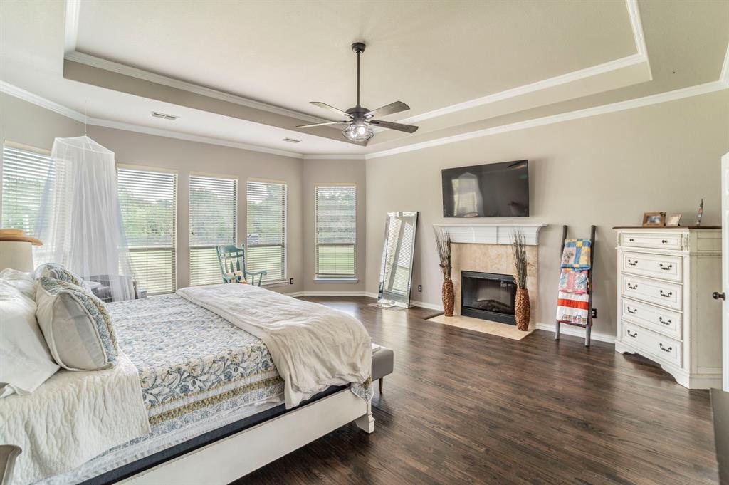 Primary Bedroom with a tray ceiling, a fireplace, dark wood-style floors, crown molding, and a ceiling fan