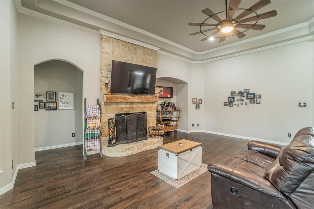 Living area with a fireplace, dark wood finished floors, crown molding, arched walkways, and a raised ceiling
