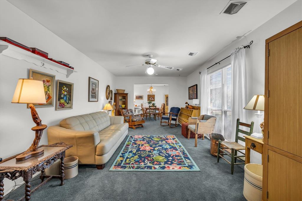 Living room with dark colored carpet, a ceiling fan, and a chandelier Living room with dark colored carpet, a ceiling fan, and a chandelier
