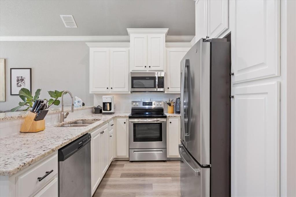 Kitchen featuring stainless steel appliances, light stone counters, white cabinets, crown molding, and light wood finished floors