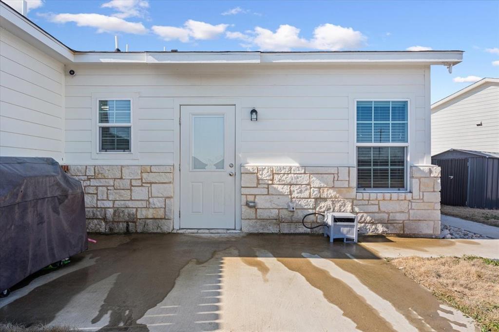 View of exterior entry featuring stone siding and a patio area