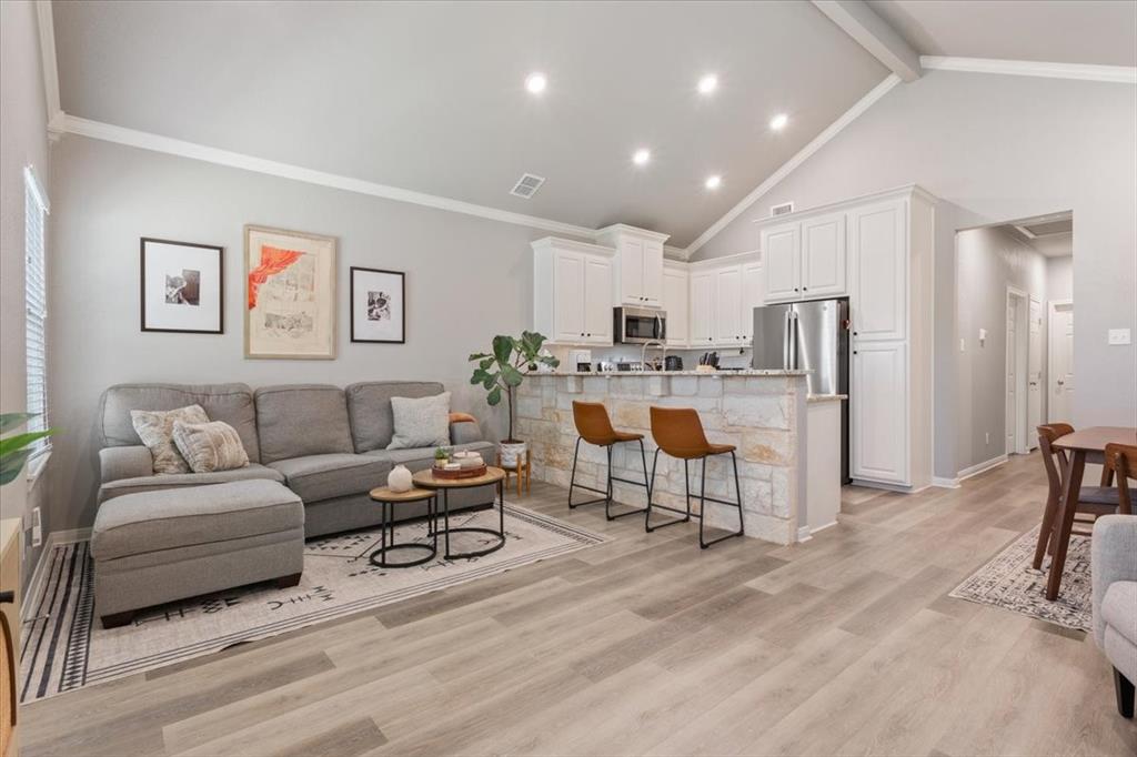 Living area featuring ornamental molding, high vaulted ceiling, light wood-type flooring, and beam ceiling