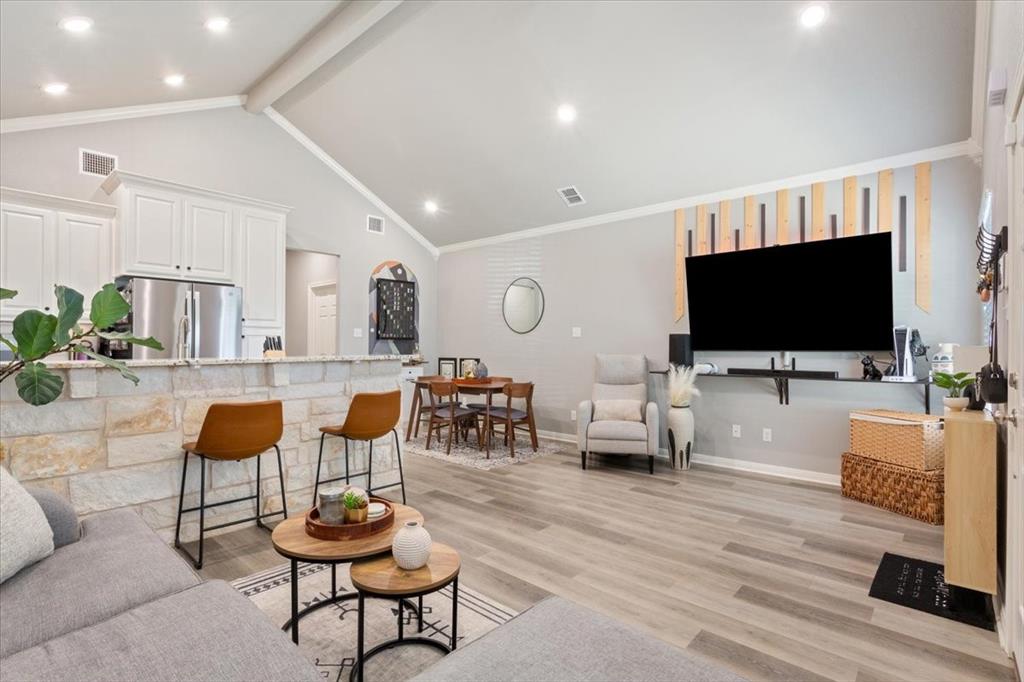 Living room featuring light wood finished floors, beamed ceiling, recessed lighting, ornamental molding, and high vaulted ceiling