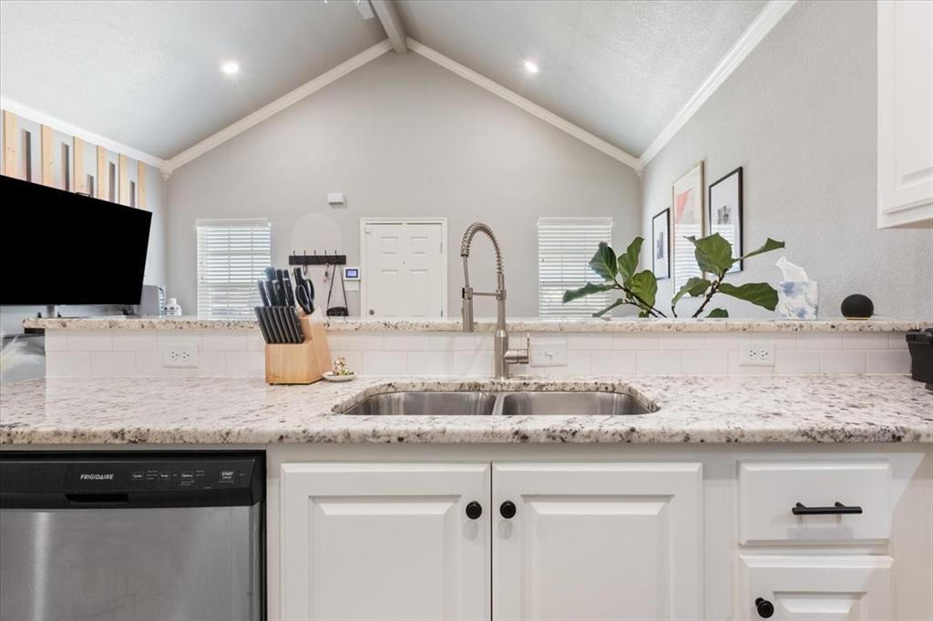 Kitchen with dishwasher, light stone counters, white cabinetry, open floor plan, and ornamental molding