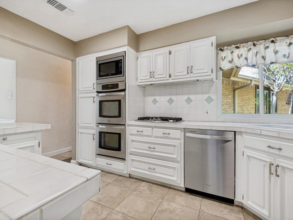 Kitchen featuring stainless steel appliances, white cabinetry, decorative backsplash, and light tile patterned floors