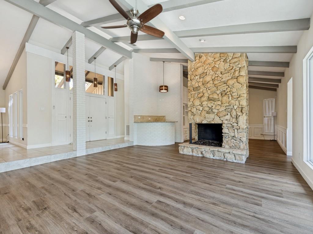 Living room with lofted ceiling, a ceiling fan, light wood-style flooring, and a stone fireplace