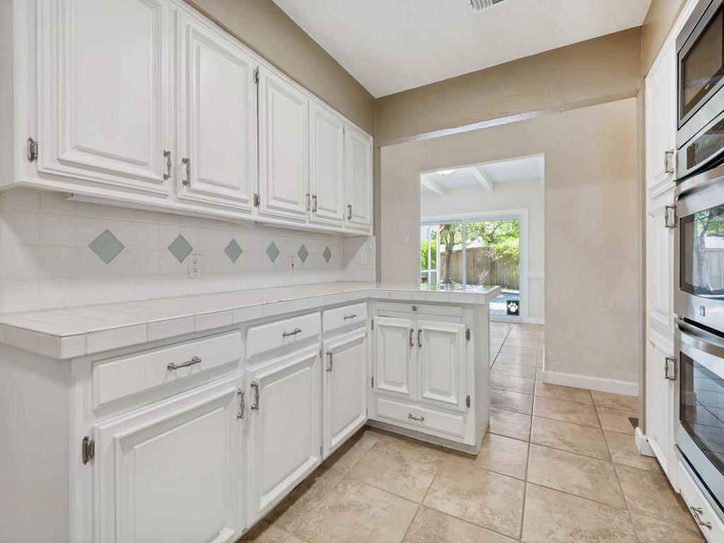Kitchen featuring tile counters, white cabinetry, backsplash, stainless steel appliances, and light tile patterned floors