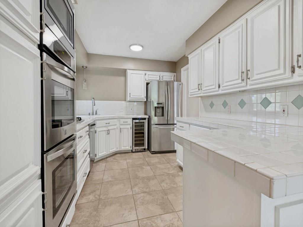 Kitchen with a peninsula, white cabinetry, stainless steel appliances, beverage cooler, and tasteful backsplash