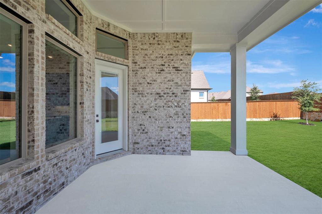Expansive covered patio featuring a concrete surface, white support columns, and a brick exterior facade
