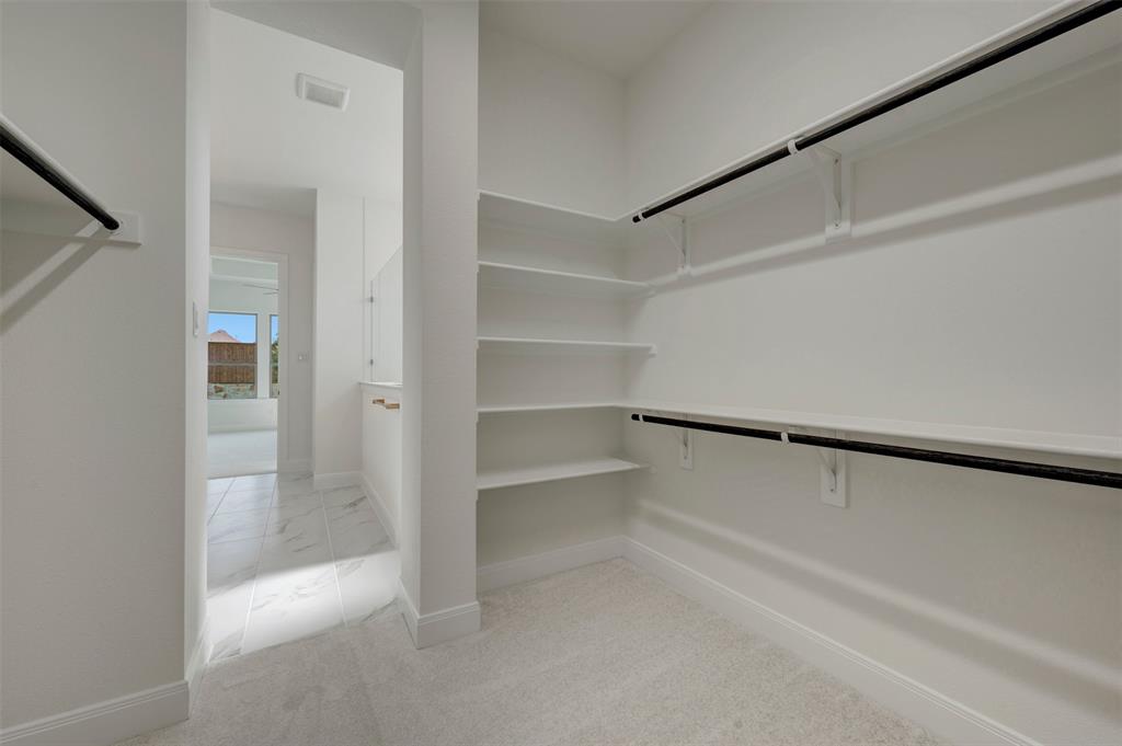 Spacious walk-in closet featuring extensive built-in shelving, dual hanging rods, light-toned carpeting, and crisp white walls
