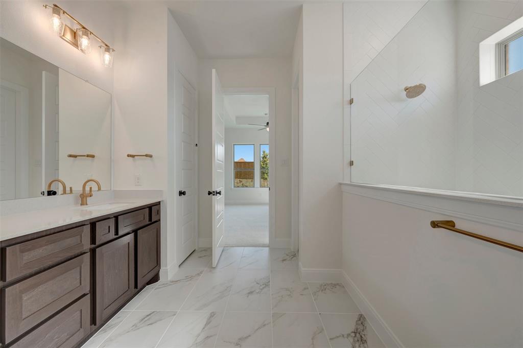Bathroom featuring a dual vanity with a white countertop and bronze-finish faucets, bronze-finish wall lighting, a large vanity mirror, and marble-look floor tiling